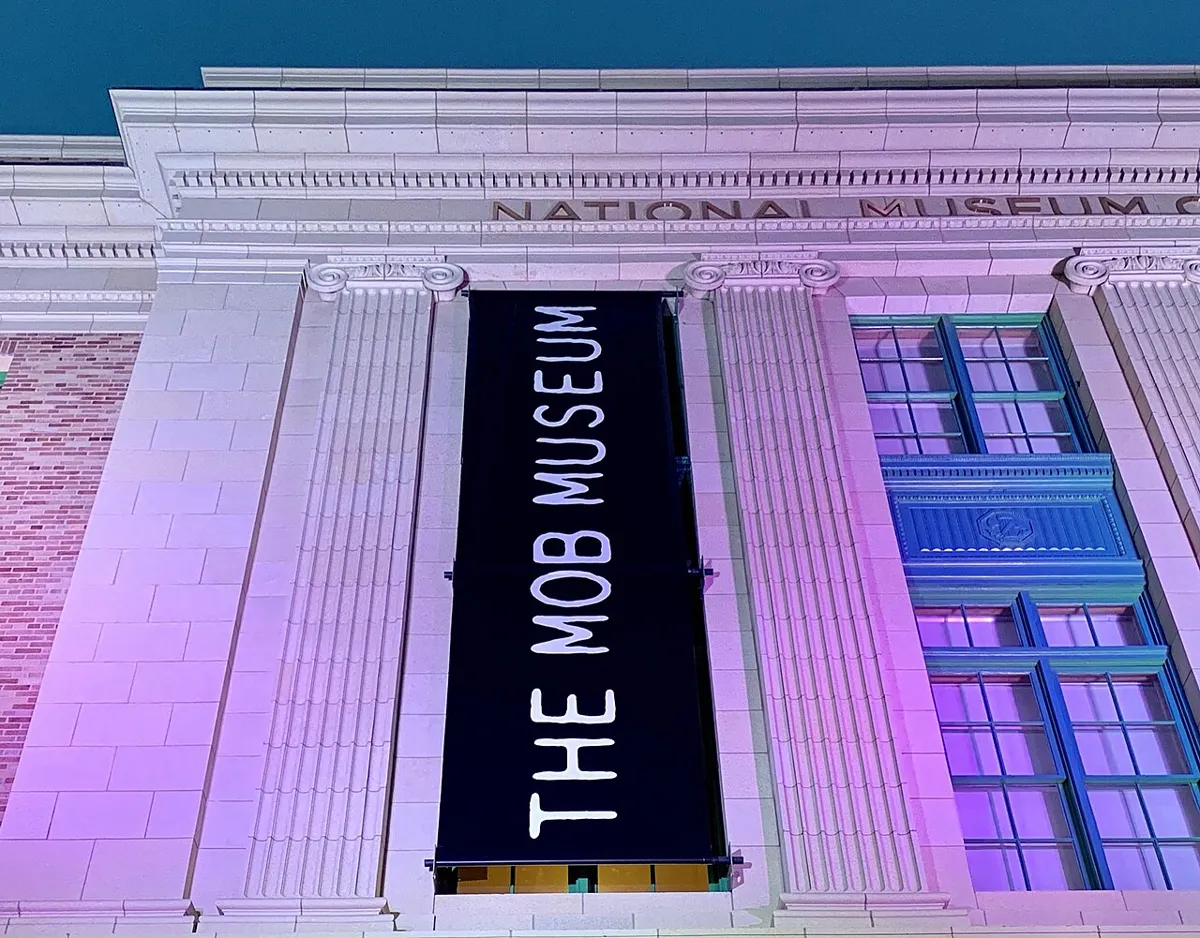 Vertical “The Mob Museum” sign between fluted columns on a stone façade illuminated in purple and blue.