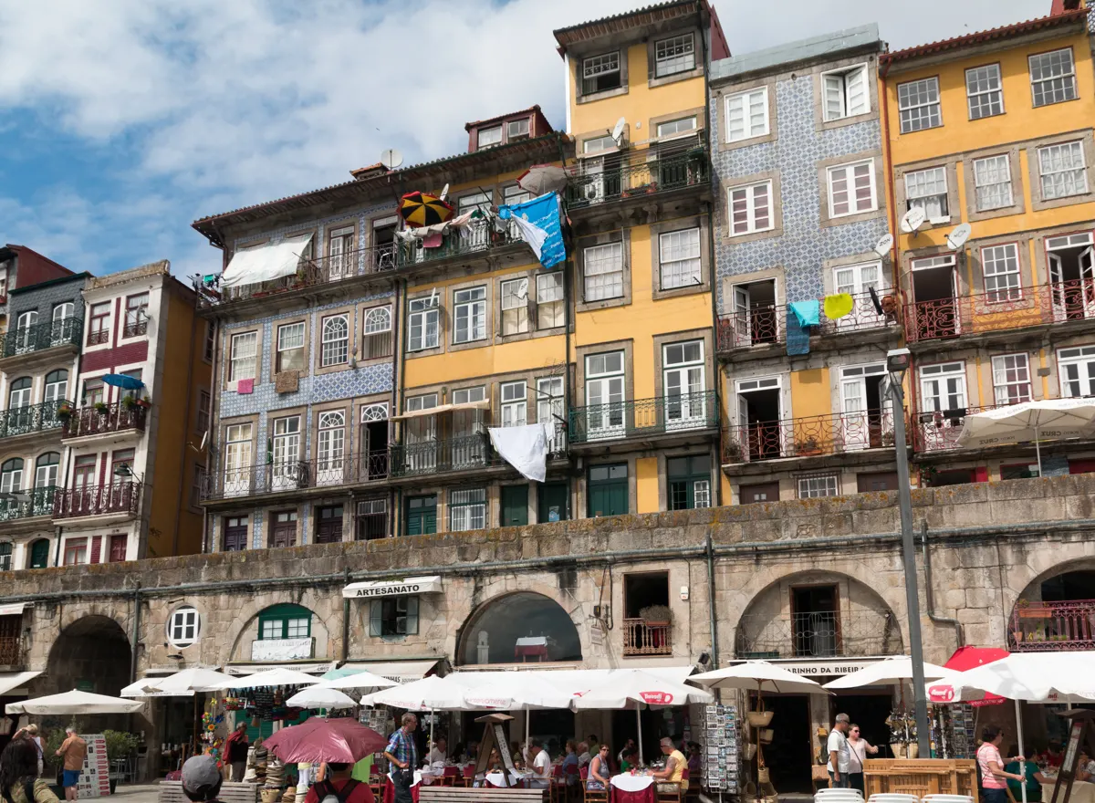 Colourful buildings with tiled façades, balconies and café terraces beside a stone wall.