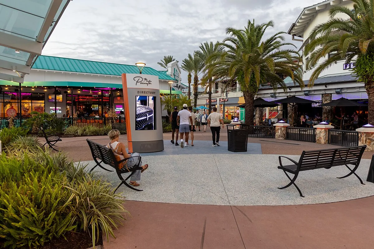 Palm-lined pedestrian plaza at Pointe Orlando, with restaurant terraces, benches and a directory sign.