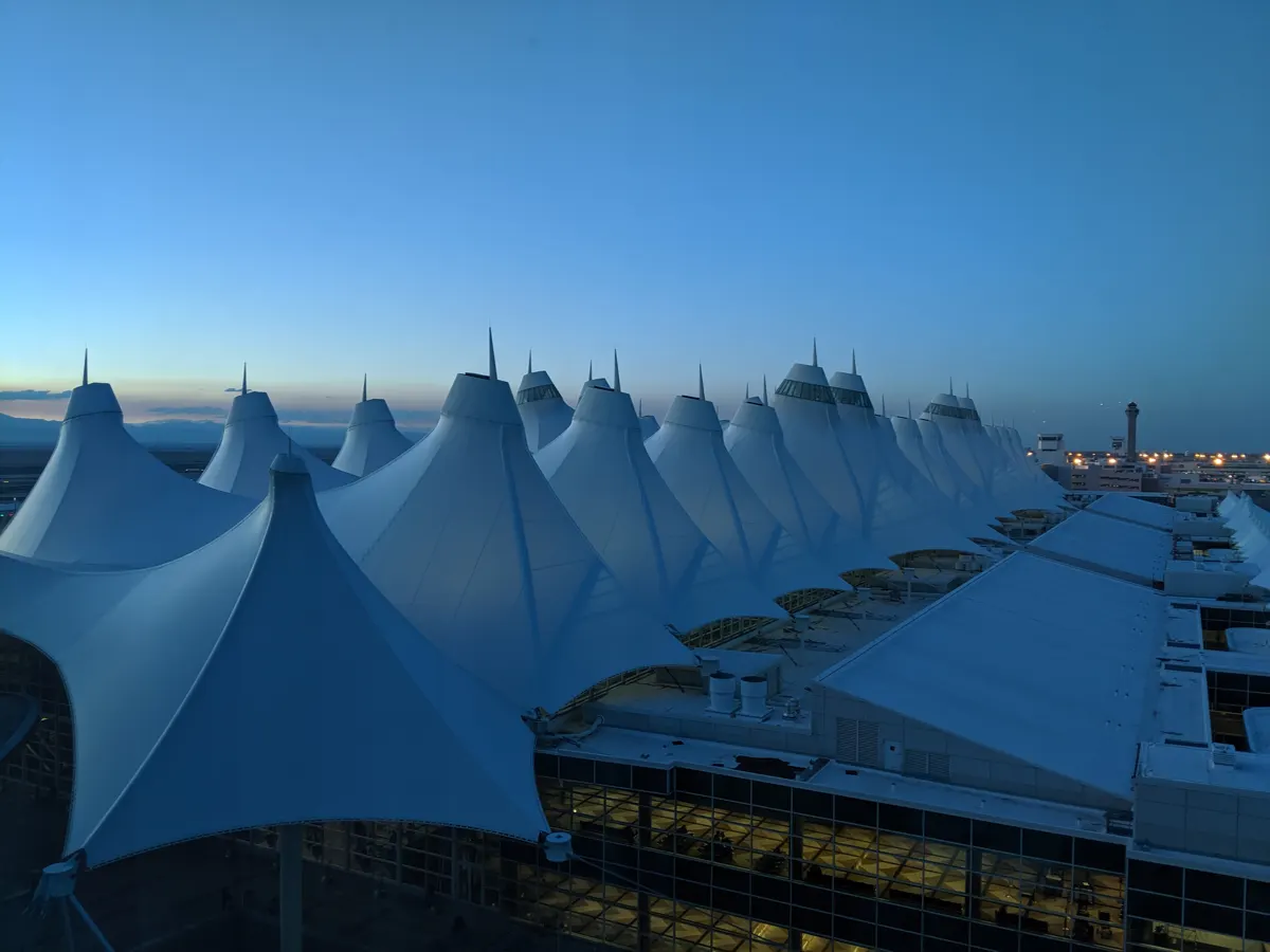 White peaked terminal roofs at dusk with illuminated windows and a distant control tower.