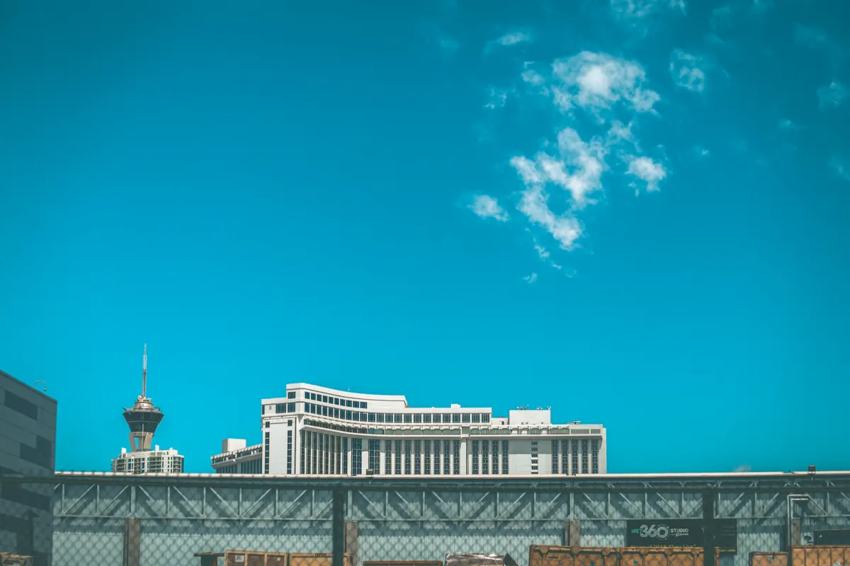 Observation tower and large buildings beneath a blue sky, with a metal structure in the foreground.