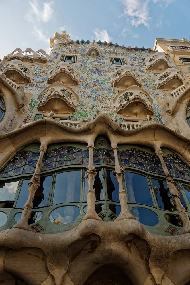 Upward view of Casa Batlló’s colourful mosaic façade, curved balconies and sculpted stone window columns.