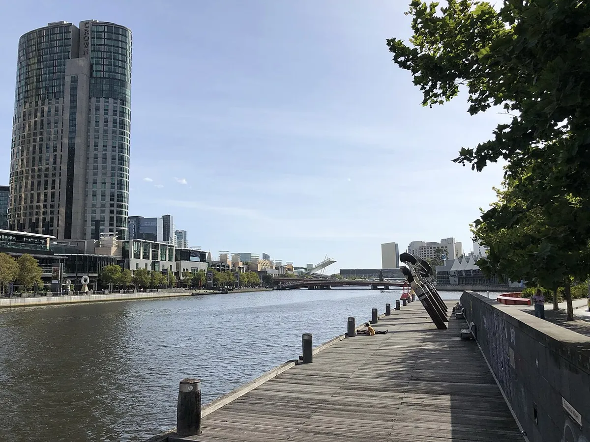 Crown Towers rising beside the Yarra River, with a wooden riverside promenade in the foreground.