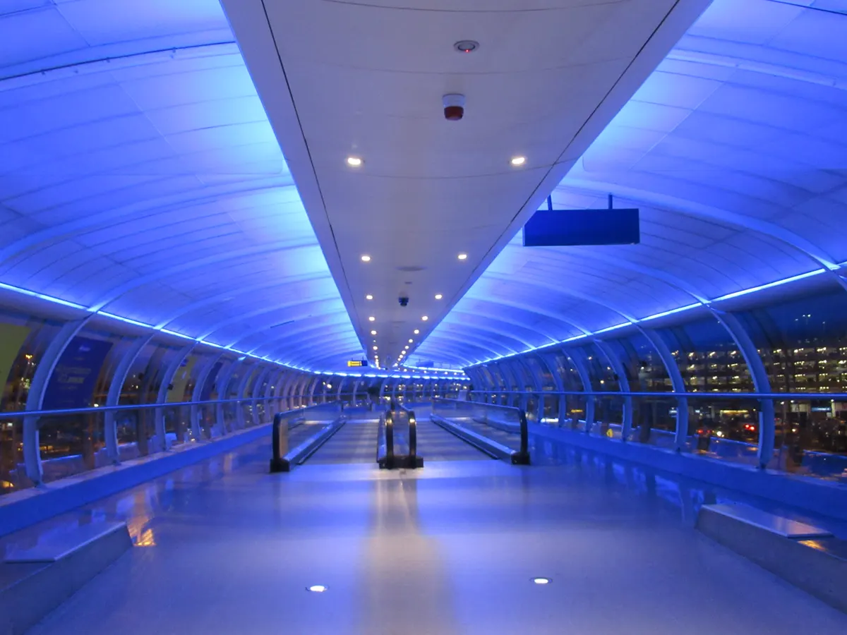 An enclosed airport walkway with moving walkways and blue lighting.