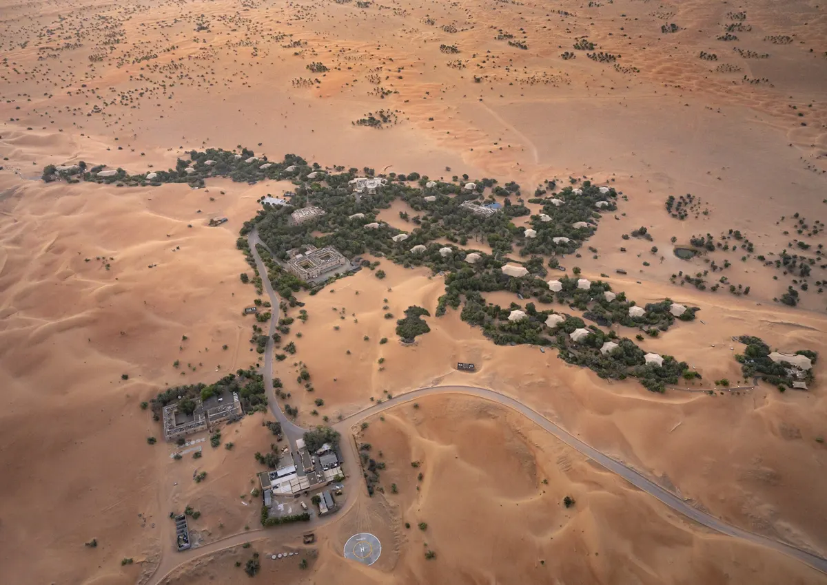 Aerial view of resort buildings among trees, winding roads and orange sand dunes.