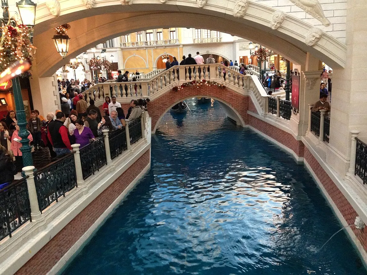 Indoor canal beneath arched bridges, with ornate façades and crowds along the railings at The Venetian in Las Vegas.